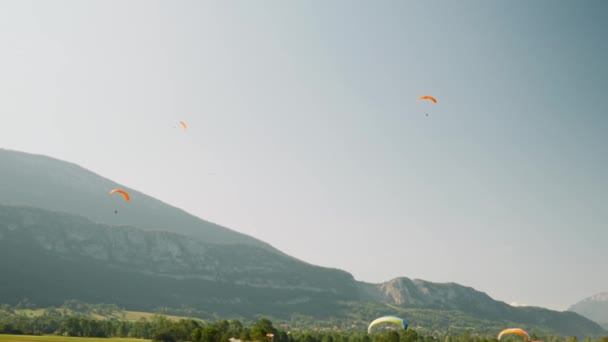 Sportive group of people fly on paragliders with blue sky and mountains on background. Paraplane runway. Flying on paraglider in Alps — ストック動画