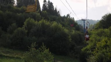 Sandalyelerdeki ziyaretçiler ağaçların arasından gökyüzü ve dağa karşı geçiyorlar. Yazın teleferik. Dağa doğru giden kadın turist Karpatlar 'daki eski teleferiğe biniyor.