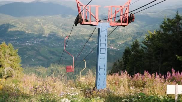 Pusty wyciąg krzesełkowy ze stalowymi kablami na szczycie wzgórza z zieloną górą na tle i błękitnym niebem. Niesamowity widok na góry z liną holowniczą stacji — Wideo stockowe