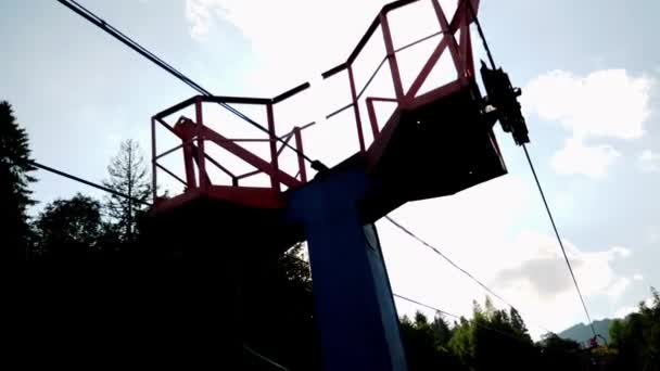 Chairlift with steel cables against sun and sky among green trees in summer. Ski lift passing through pine forest — Stock Video