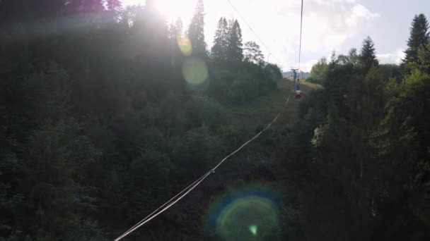 Visitantes montados em teleférico através de pinheiros que crescem na encosta da montanha. Elevador de cadeiras com cabos de aço passando em montanhas com árvores verdes no verão — Vídeo de Stock