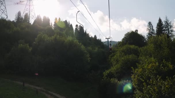 Cestující na sedačkové lanovce kolem horského průsmyku obklopeného zelenými stromy a borovicemi. Lano vlečné v zeleném lese v létě — Stock video