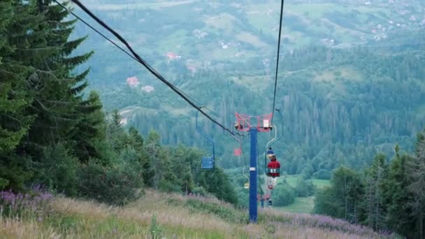 People riding on ski lift with steel rope tow in Carpathian mountains among pine trees and scotch fir on excursion at sunny summer day — Stock Video