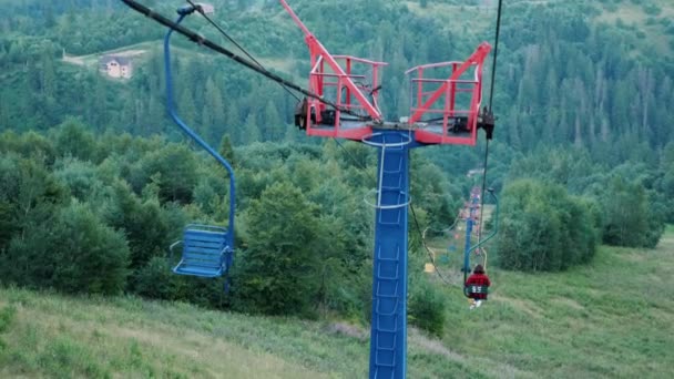 Vrouwelijke toerist rijdt op een lege stoeltjeslift met stalen touwtrekken in de Karpaten in de schemering op de zomeravond. Vrouw paardrijden op skilift tussen pijnbomen en scotch sparrenbos — Stockvideo
