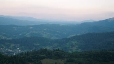 Vadideki köyde, alacakaranlıkta yeşil çam ağaçlarının arasında gün batımında ufukta güneş batarken. Yazın Karpat Dağları. Güzel dağ manzarası
