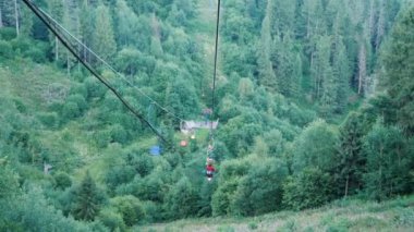 İnsanlar Karpat dağlarında kayak arabasıyla yeşil çam ormanlarından geçiyorlar. Yazın dağlarda çelik halat çekme. Dağlarda tatil