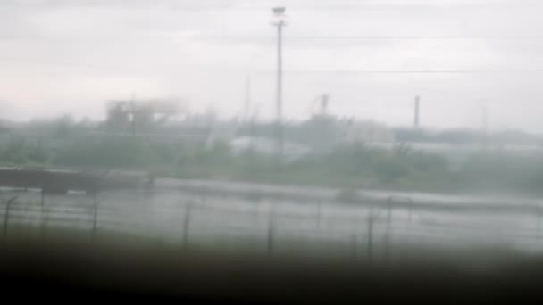 Сільський пейзаж через рухоме вікно поїзда з краплями води на склі. Падіння дощу на склі поїзда — стокове відео