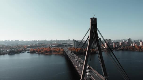 Druk autoverkeer op de brug in de grote metropool. Hoogbouw en plantenachtergrond. Drukke stadpromenade in het centrum. Betonnen brug met stalen touwtrekken. Luchtdrone zicht. Kiev, Oekraïne — Stockvideo