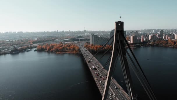 Köprüde dalgalanan Ukrayna bayrağı iki metropolü birbirine bağlıyor. Yoğun araba trafiği olan beton köprünün hava aracı görüntüsü. Nehirli güzel bir şehir manzarası olan köprünün üzerinde bir dron uçuşu. Kyiv, Ukrayna — Stok video