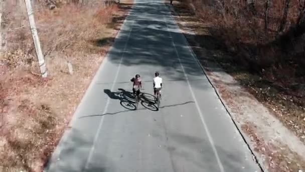 Dos ciclistas profesionales que montan en bicicletas de carretera en la carretera vacía en el parque de la ciudad de otoño en el día soleado y cálido, vista trasera seguir. Imágenes aéreas de aviones no tripulados de personas montadas en bicicletas a lo largo del bosque — Vídeos de Stock