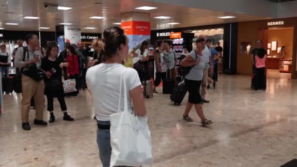Genève / Suisse - 22 juillet 2019 - personnes avec valises et bagages debout près du tableau des horaires de départ et d'arrivée à l'aéroport de Genève. Voyageurs en attente de vol en zone duty free dans la zone de départ — Video