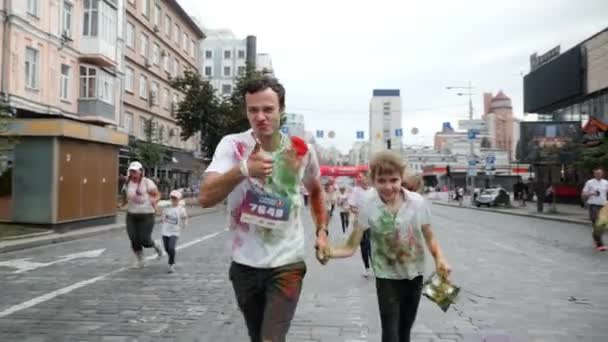 Kyiv/Ukraine - June 2, 2019 - Brother holding hand of his young sister stained in colorful fluorescent holi paint and running on street in city center at Color Run — Stock Video