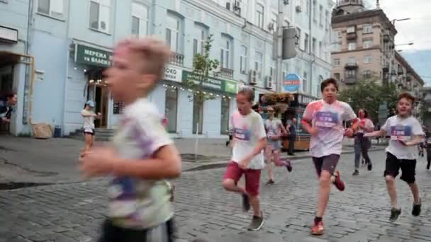 Kyjev / Ukrajina - 2. června 2019 - Happy children in white t-shirt are smered fluorescent colorful holi paint running on street in city center at Color Run — Stock video