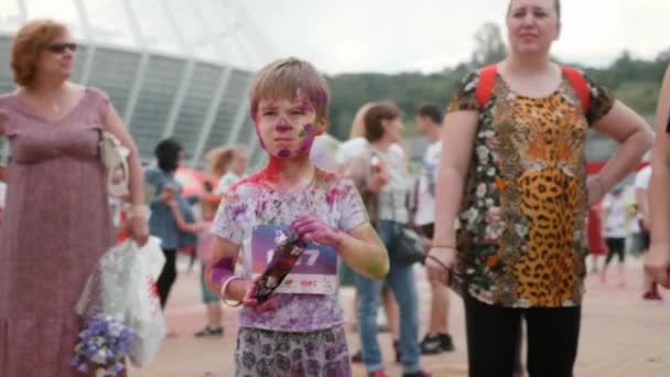 Kiev / Ukraina - 2 juni 2019 - Charmig ung pojke färgad i färgglada fluorescerande färg står på ruta efter ras Color Run Kiev och håller paket holi färg för färgfestival — Stockvideo