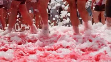 Spor ayakkabılı kadın ve erkek ayakları boya festivalinde köpükle koşuyor. Renkli floresan Hint Holi boyalarıyla lekelenmiş bacaklar şehir merkezinde köpükten akıyor.