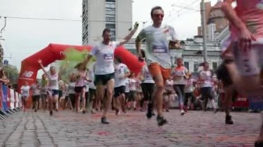 Kyiv / Ukrayna - 2 Haziran 2019 - Beyaz tişörtlü çekici kadın ve erkekler Hintli holi boyaları başlangıç çizgisini geçiyor ve Color Run 'daki boya festivalinde şehir merkezinde koşmaya başlıyor