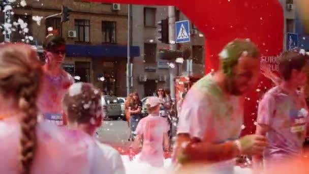 Kiev / Ucrânia - Junho 2, 2019 - Pessoas felizes em camisetas brancas manchadas em tintas coloridas fluorescentes holi jogging sob arco inflável e espuma, rindo e se divertindo na Color Run — Vídeo de Stock