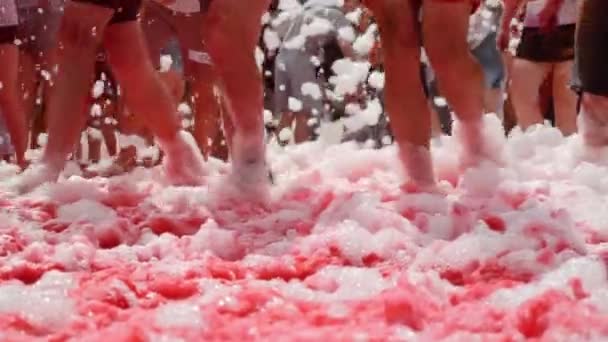 Female and male feet in sneakers are jogging on foam at paints festival. Legs stained in colorful fluorescent indian holi paints running through foam in city center — Stock Video
