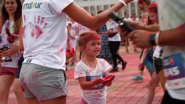 Kiev / Oekraïne - 2 juni 2019 - Klein schattig meisje in witte kleding is besmeurd kleurrijke verven houden in handen fluorescerende holi verf op Color Run — Stockvideo