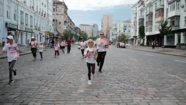 Κίεβο / Ουκρανία - 2 Ιουνίου 2019 - Γοητευτικό χαμογελαστό κοριτσάκι με γυαλιά ηλίου, λευκό t-shirt και μαντίλα χρωματίζεται σε πολύχρωμες μπογιές holi που τρέχουν σε πλακόστρωτες πέτρες κατά μήκος του κέντρου της πόλης στο φεστιβάλ χρωμάτων — Αρχείο Βίντεο
