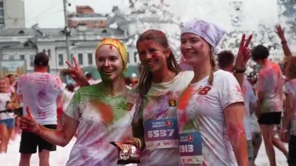 Kiev / Oekraïne - 2 juni 2019 - Drie aantrekkelijke lachende vrouwen in witte t-shirts besmeurd kleurrijke fluorescerende holi verf nemen van foto 's en poseren voor de camera en het doen van "vrede" door de handen op Color Run — Stockvideo