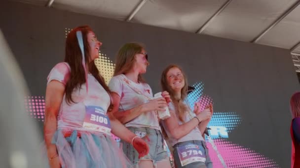 Kiev / Oekraïne - 2 juni 2019 - Jonge aantrekkelijke vrouwen besmeurd kleurrijke indiase holi verf in grappige kostuums staan op het podium en deelnemen aan de wedstrijd op Color Run — Stockvideo