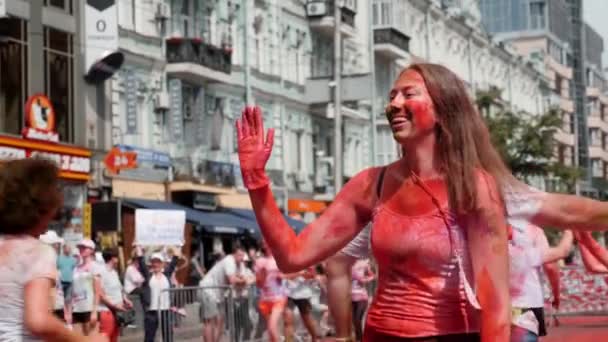 Kiev / Ucrânia - 2 de junho de 2019 - Happy charming young woman smeared colorful fluorescent indian holi paints gives five to people passing by at Color Run and laughing — Vídeo de Stock