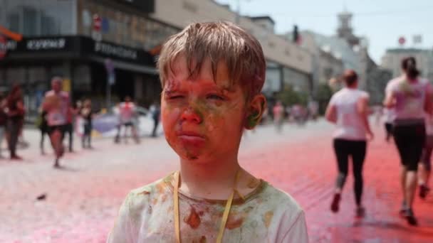 Kyiw / Ukraine - 2. Juni 2019 - Portrait des süßen, charmanten kleinen Jungen mit verschmiertem Gesicht, bunte fluoreszierende indische Holi-Farben beim Farbenfest beim Farbenlauf — Stockvideo