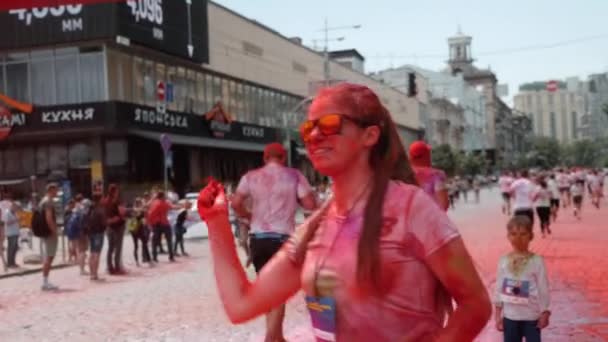 Kyiv / Ukraine - June 2, 2019 - Νεαρή ευτυχισμένη μελαχρινή γυναίκα με γυαλιά ηλίου και λευκό t-shirt απλώνει πολύχρωμα φθορίζοντα ινδικά χρώματα holi σε ανθρώπους που τρέχουν στο Color Run — Αρχείο Βίντεο
