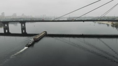 Şehir merkezindeki dolu köprüden geçen boş sakin nehirde yüzen kumlarla dolu bir mavna. Sanayileşmiş şehirde yoğun siste seyreden gemi, hava aracı atışı.
