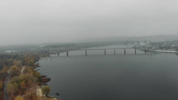 Metrópolis en smog industrial. Drone volando sobre amplio río tranquilo y bosque caducifolio con el centro de la ciudad en la niebla en el fondo, vista aérea del dron — Vídeo de stock