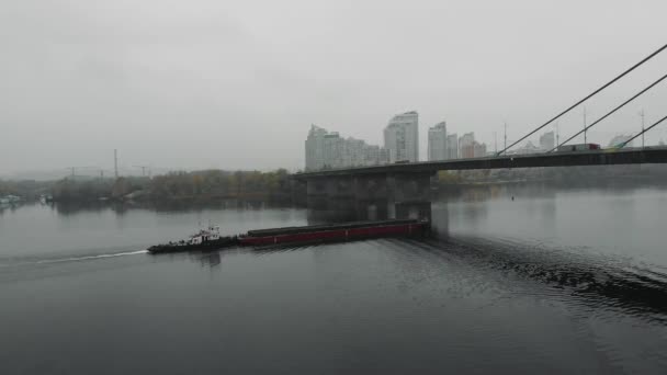 Pequeño remolcador con scow está navegando en el ancho río tranquilo en smog industrial. Barcaza mayor flotando en la niebla en el arroyo a través de puente de hormigón en el centro — Vídeo de stock