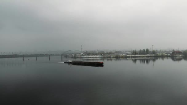 Железная баржа, плывущая по пустой спокойной реке через промышленный смог в центре города. Большая скотина, плывущая по мосту в центре города в тумане, воздушный дрон выстрел — стоковое видео