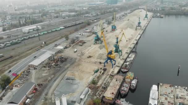 Вид с воздуха на портовые рабочие краны, добывающие песок с железной баржи и добывающие его на берегу реки в промышленном грязном городе в смоге — стоковое видео