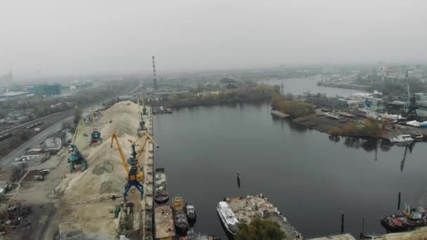 Vista aérea da cidade cinzenta industrial coberta de nevoeiro e nevoeiro. Trens de carga e estação ferroviária perto de docas fluviais e guindastes portuários de carga — Vídeo de Stock