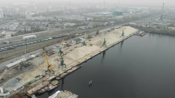 Кран собирает щебень и песок с баржи во время работы в порту. Промышленный город со смогом . — стоковое видео