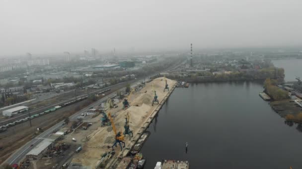 Guindastes portuários descarregando areia do rio da barcaça em docas com escavadoras e caminhões se movendo. Conceito de docas industriais — Vídeo de Stock