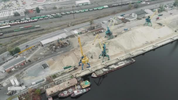 A pile of sand and cargo working cranes with excavators moving river sand in docks. Industrial part of city with cargo trucks and tractors working — Stock Video