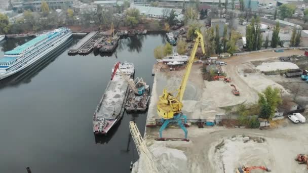 Чотири робочі промислові крани в доках біля купи піску, що рухають пісок від баржі до вантажівок. Промислове місто з туманом і смогом — стокове відео