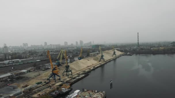 Vista aérea de la ciudad industrial en niebla y niebla con grúas de construcción trabajando en muelles. Barcaza de arena y camiones que transportan arena . — Vídeos de Stock