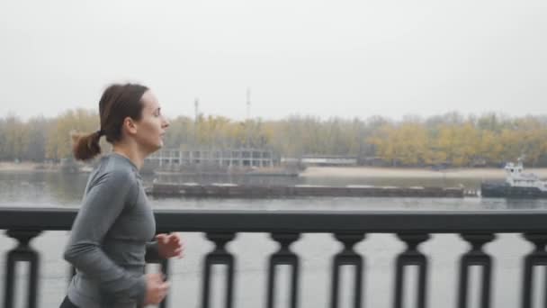 Motivasyonlu formda sporcu kadın, şehrin sanayi bölgesinde nehir boyunca yoğun bir nefes alma ve eğitim görüyor. Genç profesyonel bayan koşucu günlük antrenman yapıyor ve kilo vermek için koşuyor — Stok video