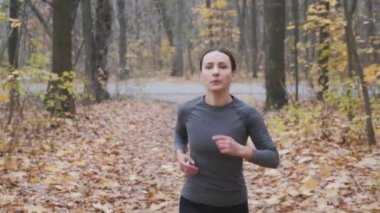 Parkta koşan siyah ve gri giysili spor elbiseli kadın. Ormanda koşan motive bir kadın.