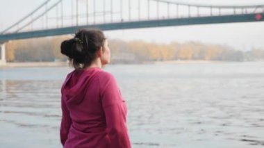 Siyah ve menekşe rengi spor giysiler giymiş, İskandinav yürüyüş direkleri olan tombul kadın eğitimini takip edin.