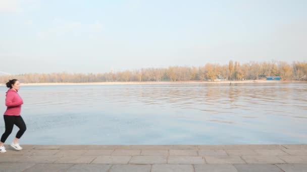 Young motivated female doing an easy jogging along industrial city river while training for marathon — Stock Video