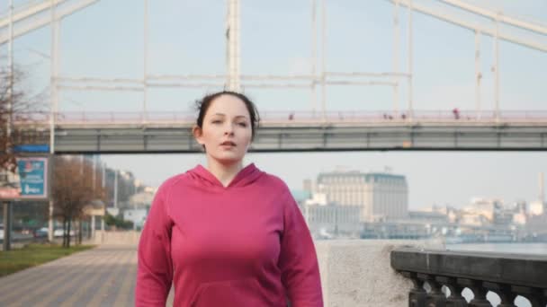 Fronte seguire colpo di signora attraente facendo nordic walking formazione in città lungo il fiume e ponte della città. Concetto benessere — Video Stock