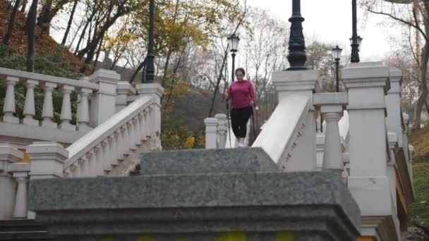 Mujer joven motivada haciendo entrenamiento nórdico caminando subiendo y bajando las escaleras de la ciudad. Concepto de bienestar — Vídeos de Stock