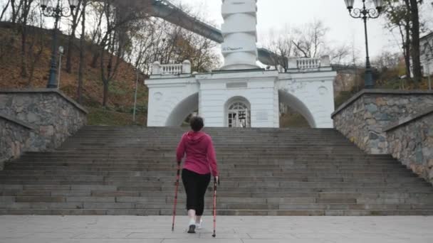 Молода пухка приваблива жінка піднімається по сходах з полюсами для скандинавської ходьби. Концепція втрати ваги — стокове відео