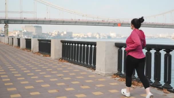 Jonge, schattige vrouw die 's morgens alleen de rivier in rent. Training voor marathonwedstrijden — Stockvideo