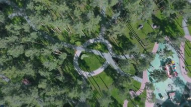 Çocuk parkı, yaya yolları, bisiklet yolları, yeşil çimenler ve havadan manzaralı modern şehir parkı. Güneşli yaz gününde yeşil çam ağaçları olan güzel şehir parklarının insansız hava aracı görüntüleri.