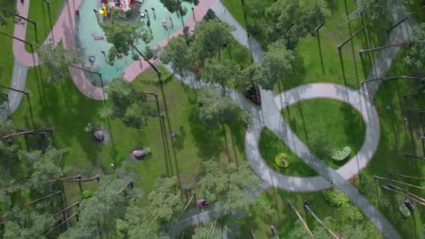 Unglaublicher Blick von oben auf den modernen Stadtpark mit Kinderspielplatz, Fuß- und Radwegen, Bänken und Menschen, die sich an sonnigen Sommertagen ausruhen — Stockvideo